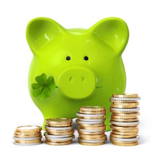 Green piggy bank with clover and coin stacks
